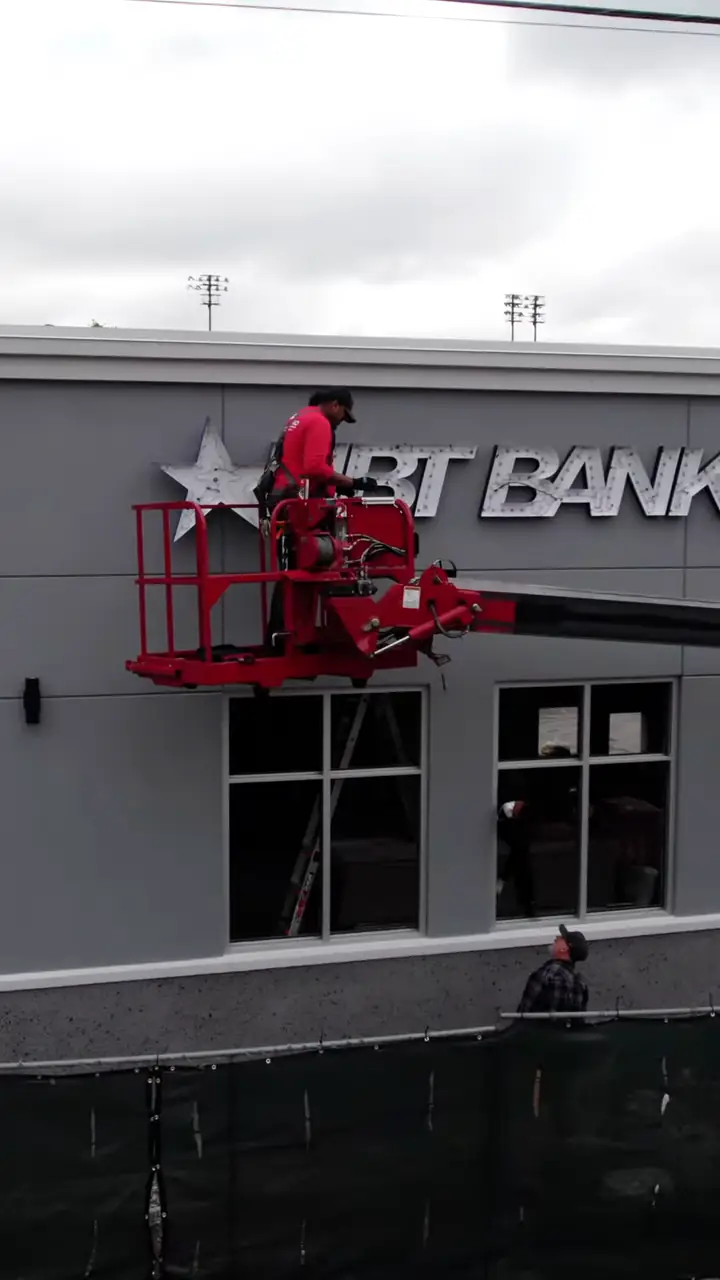A crew in a lift mounting NBT Bank channel letters on a building