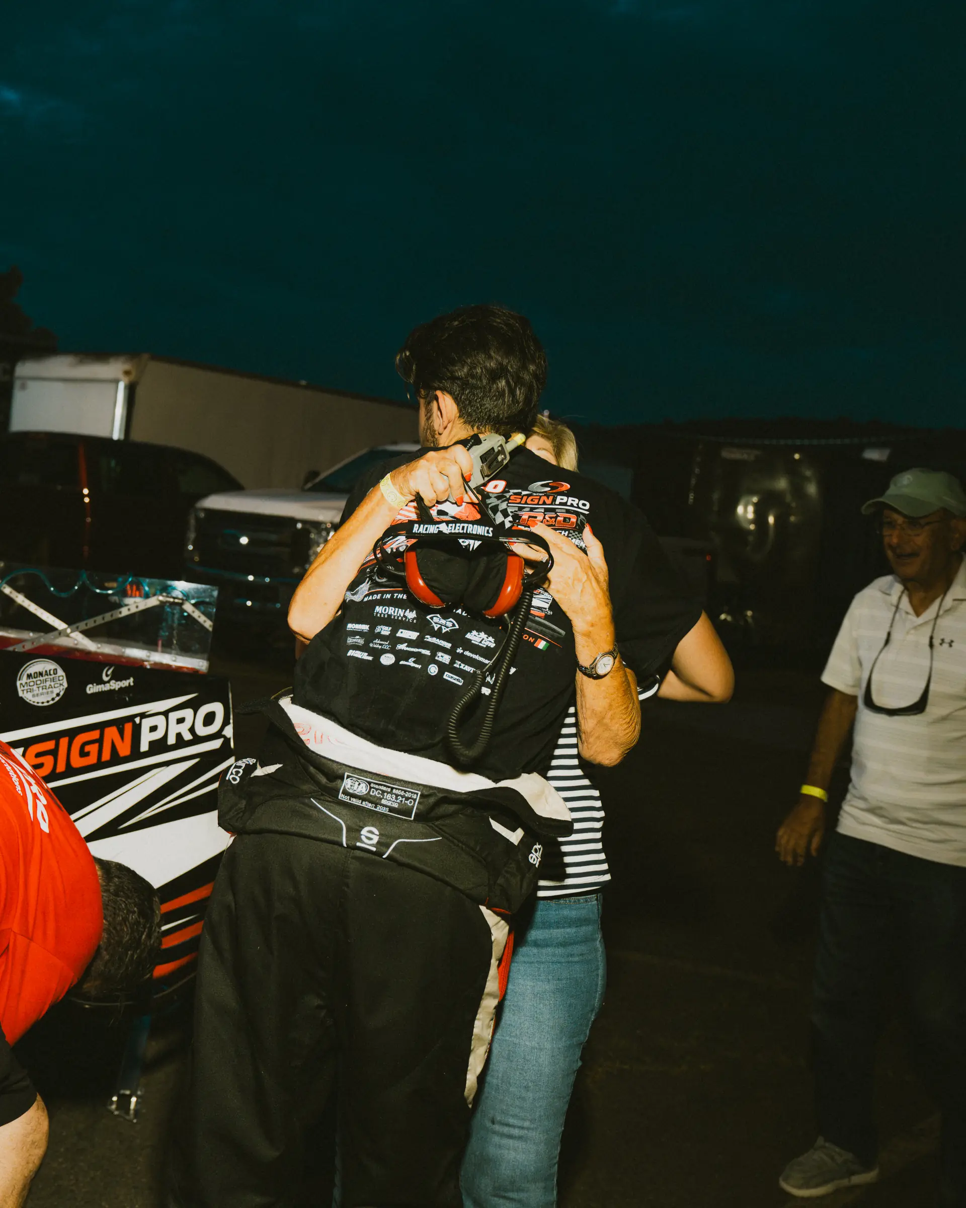 A trackside embrace beside the Sign Pro car